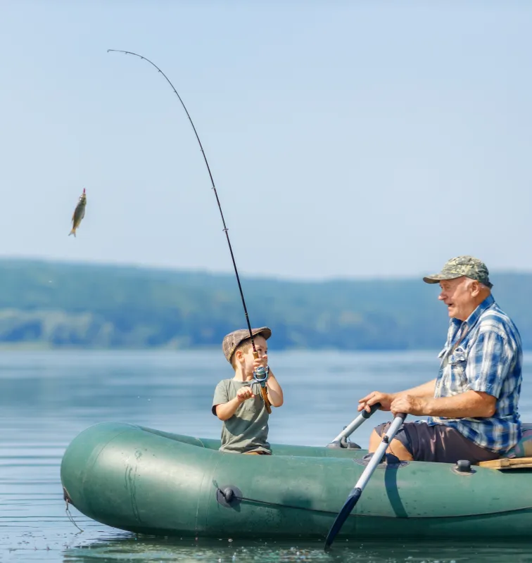 A grandfather and grandson were happily fishing from an inflatable boat on the lake